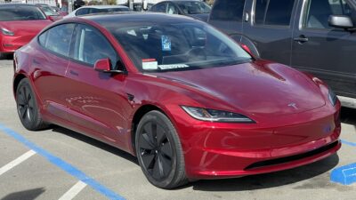Piros Tesla Model 3 egy parkolóban, elölről és oldalról
