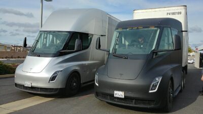 Két Tesla Semi prototípus, egy ezüst és egy sötét kamion egymás mellett